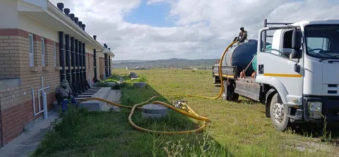 Water service vehicle and hoses beside a construction site