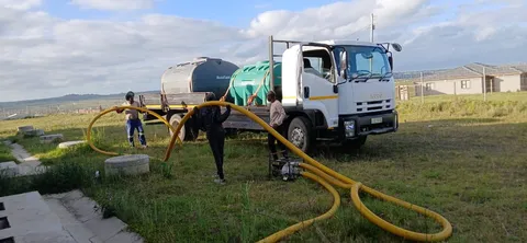 Water service vehicle and hoses beside a construction site