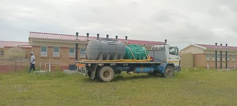 Water service vehicle and hoses beside a construction site