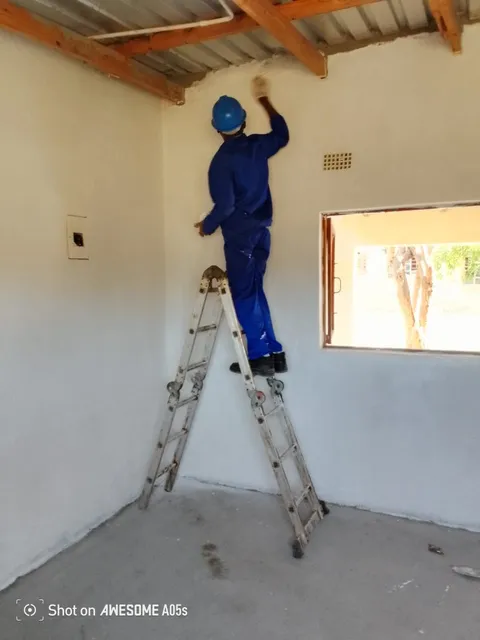 Worker finishing an interior wall from a ladder